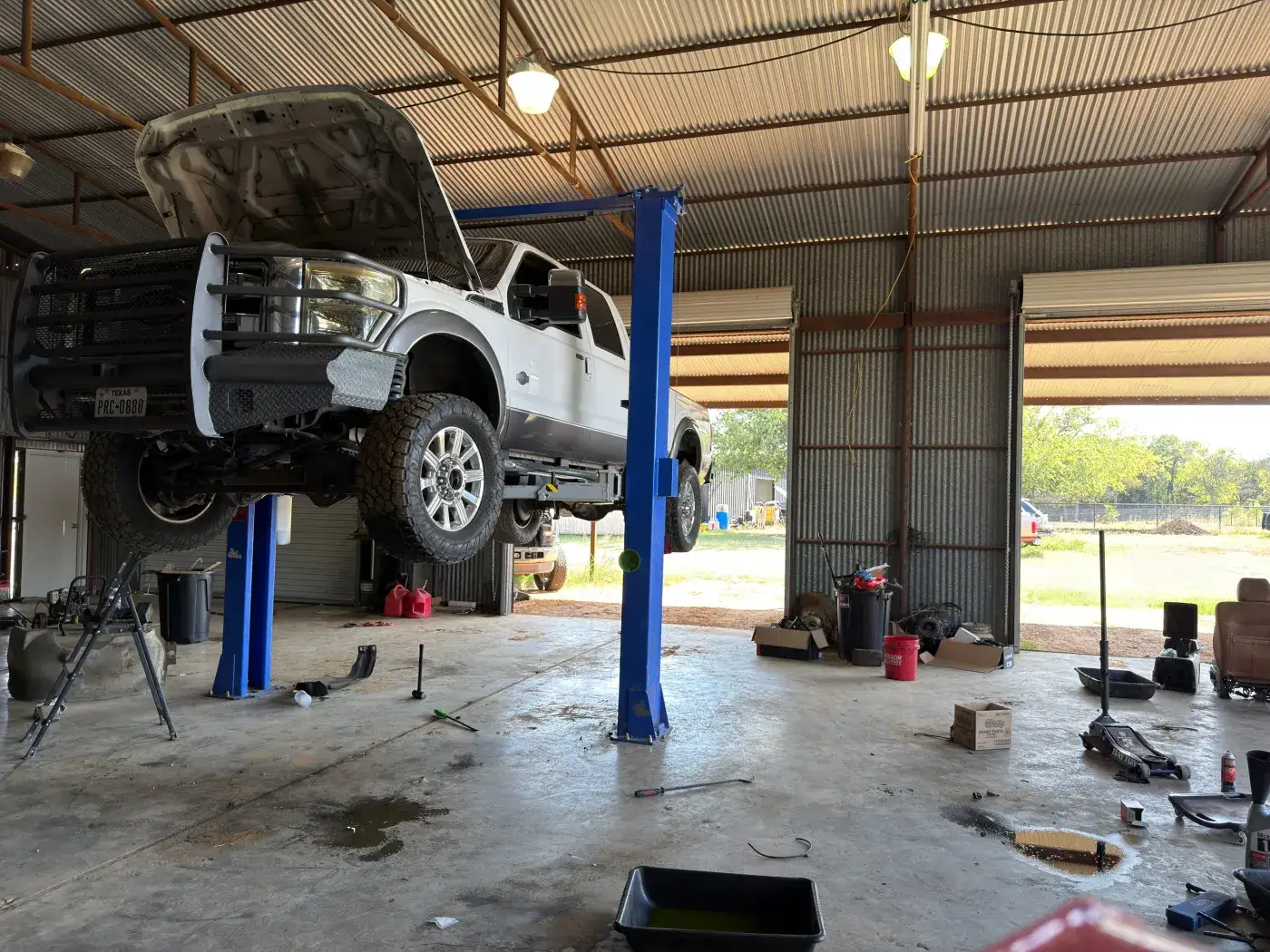 A diesel pickup raised on a two-post lift in the open bay at Young Motorsports in Alvarado, Texas
