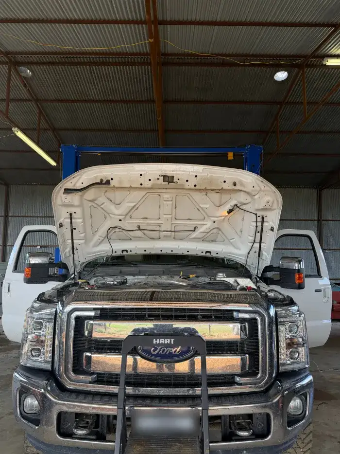 A white Ford Super Duty with the hood up on a two-post lift at Young Motorsports